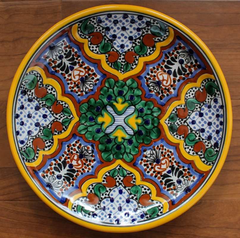 Hand-painted Talavera pottery plate with vibrant traditional Mexican floral and geometric designs in green, yellow, blue, and orange colors